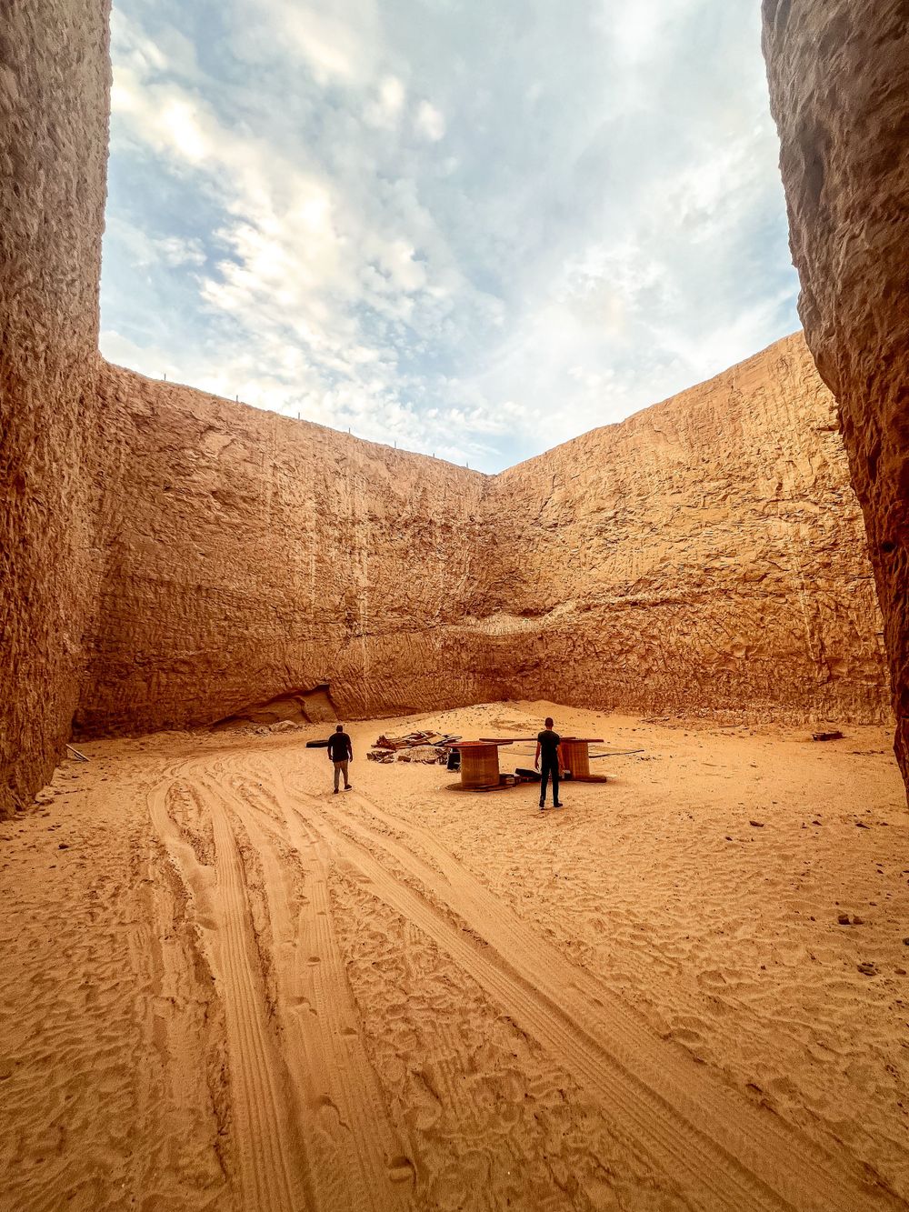 Military personnel stand in a sandy quarry surrounded by high earthen walls under a cloudy sky.