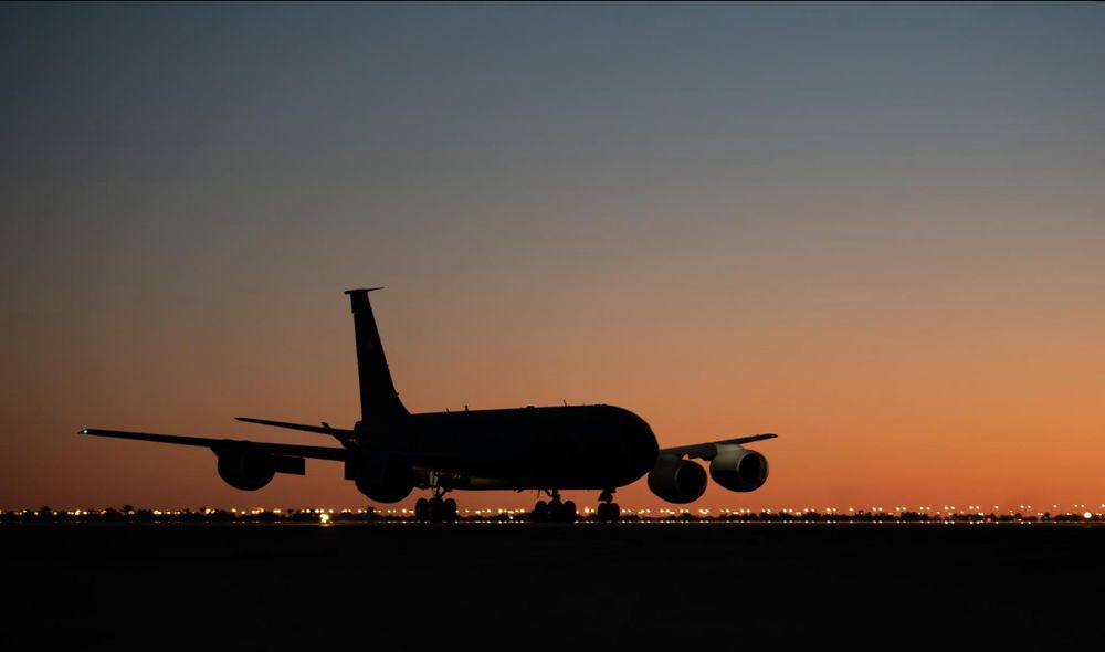 Military aircraft silhouetted against an orange sunset sky on runway.