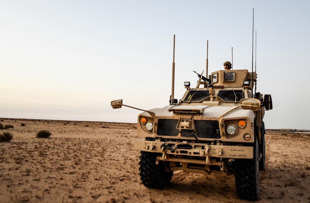 Tactical military vehicle positioned in desert terrain during sunset.