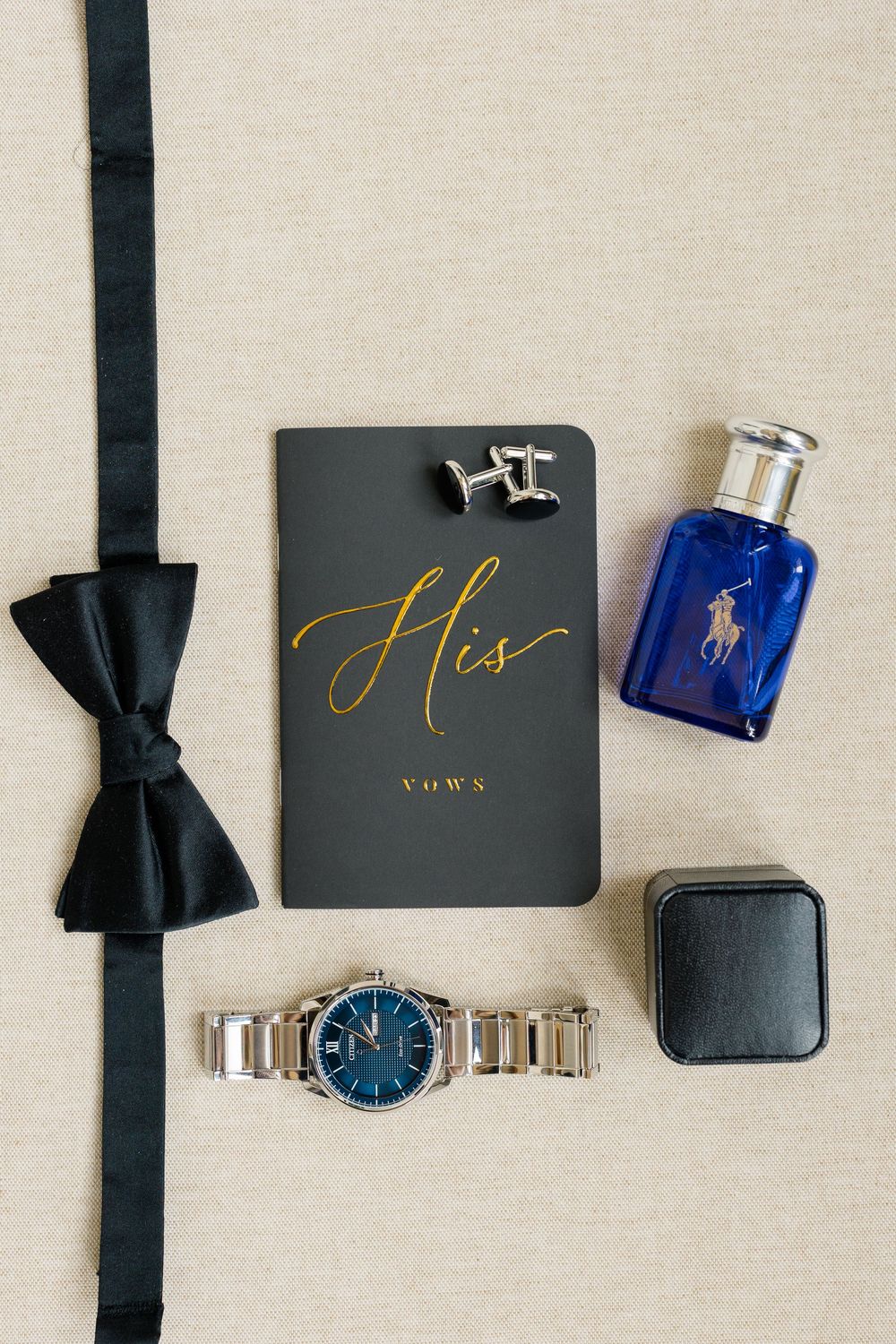 Groom wedding flat lay with black bow tie, vow book, cufflinks, Ralph Lauren cologne, watch, and ring box.