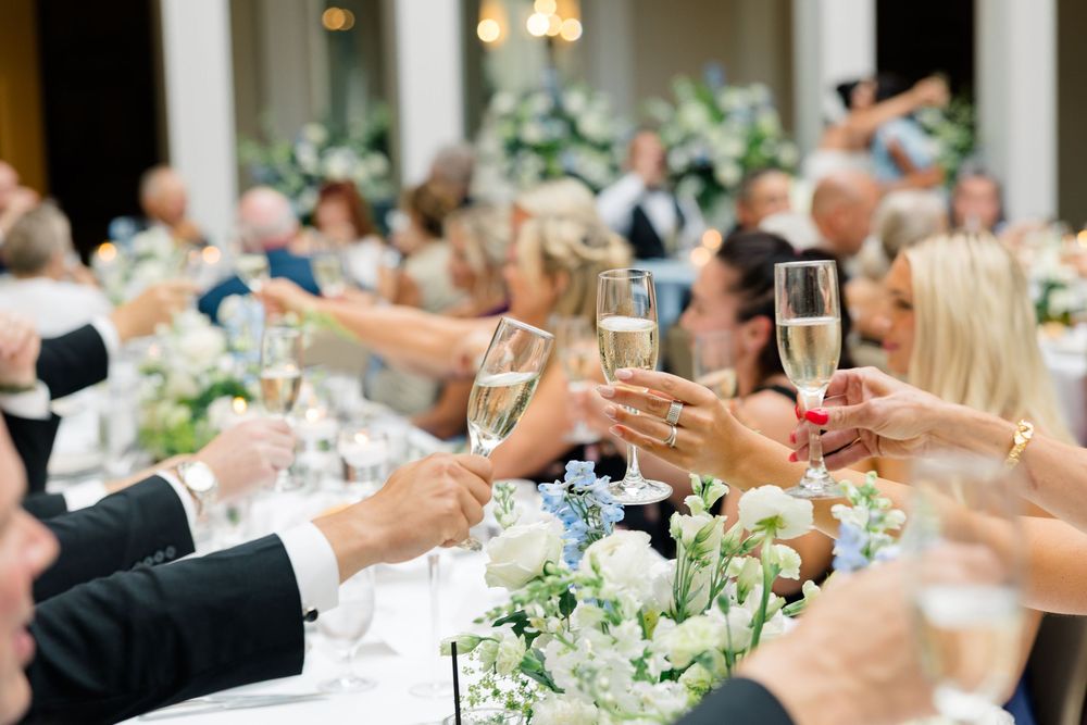 Guests raising champagne glasses in a toast at an elegant wedding reception with floral centerpieces.