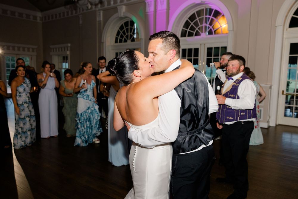 Bride and groom share their first dance at elegant wedding reception with guests watching in background.