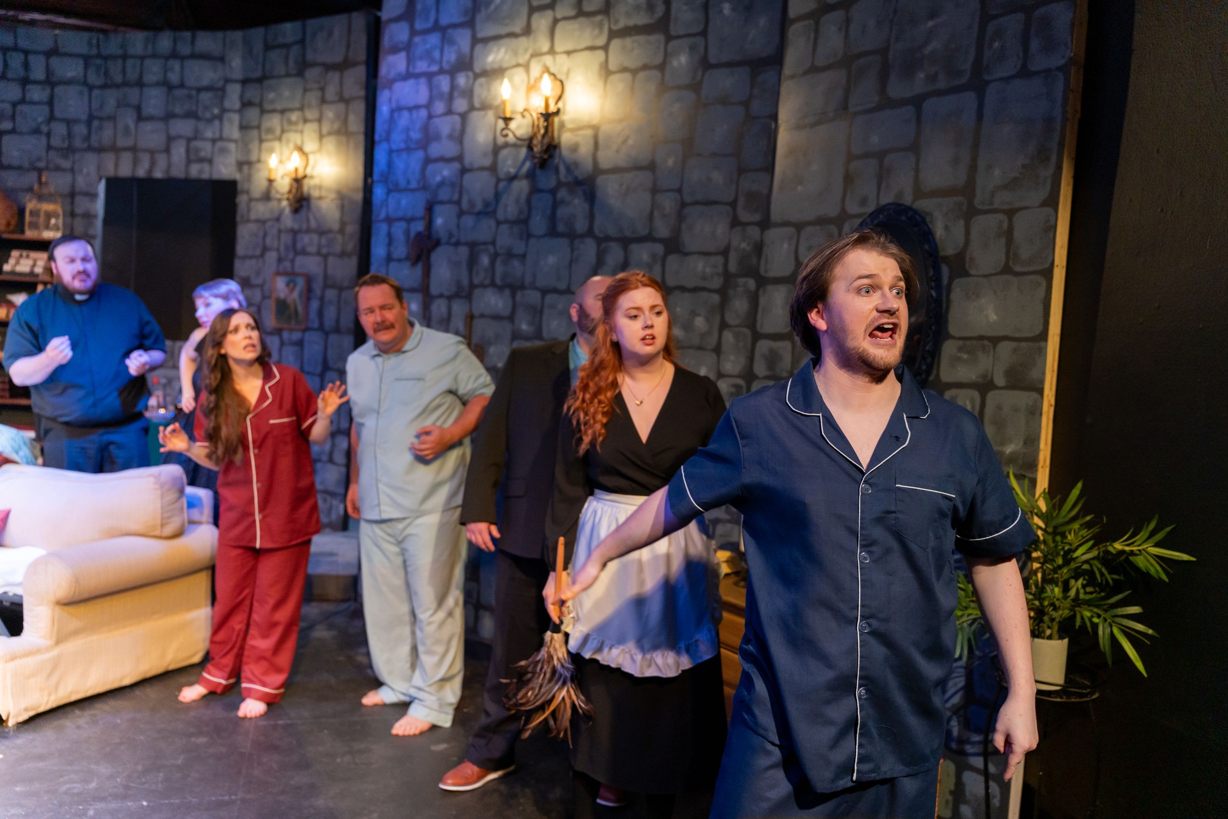Group of performers react energetically on stage with stone wall backdrop in theatrical production.