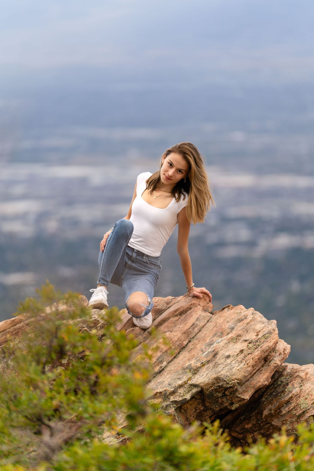 Candid pose on rocky mountain overlook with city vista in background.