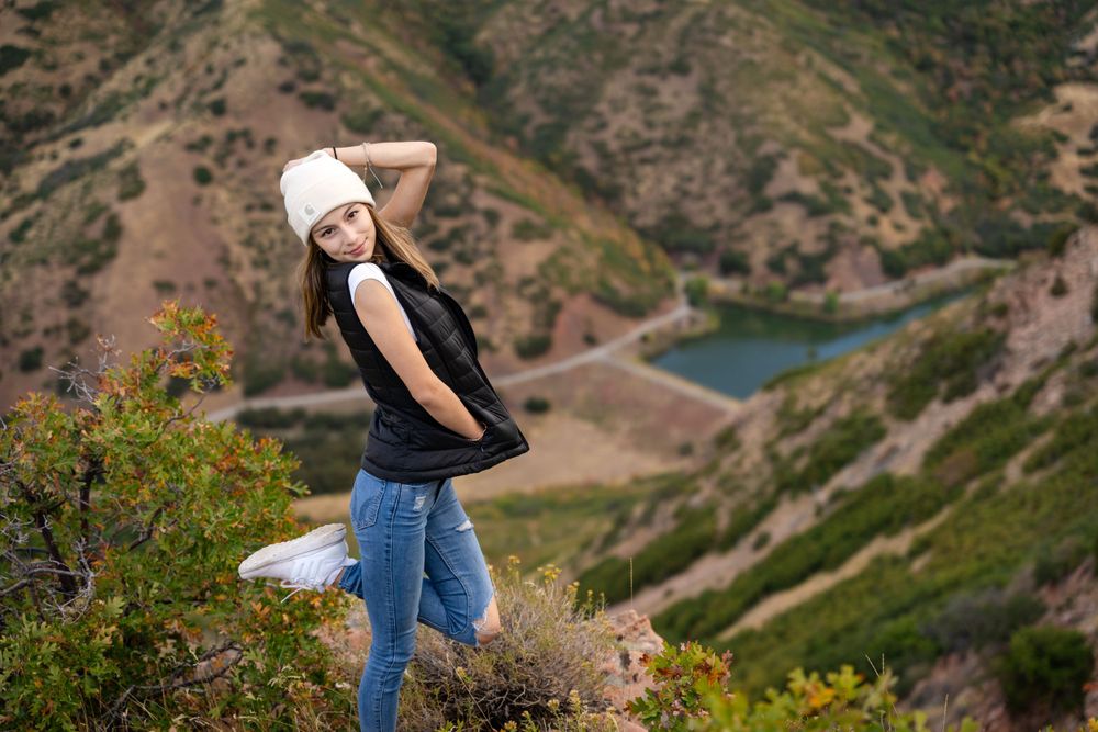 Playful mountain-top portrait with turquoise alpine lake visible in valley below.