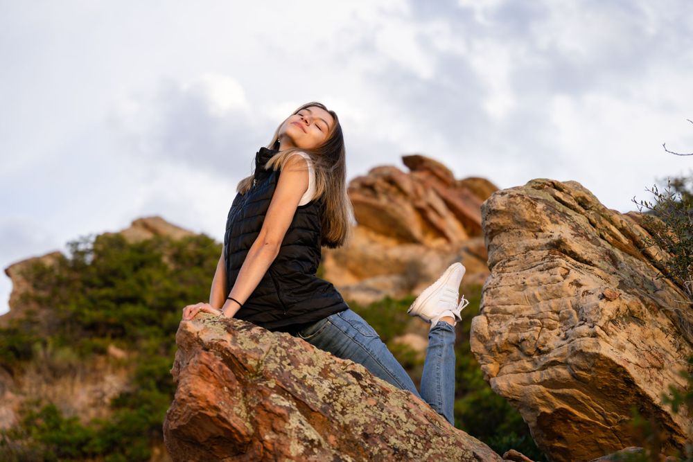 Carefree pose on rocky outcrop against dramatic mountain landscape.