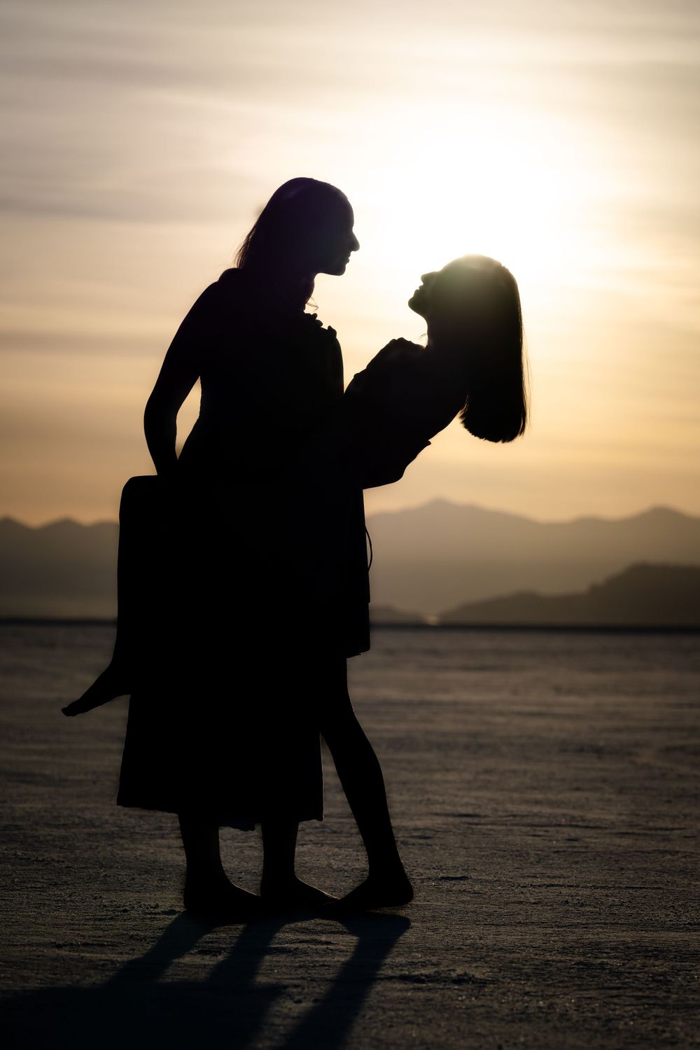 Romantic silhouette couple dancing at sunset with mountains in background.