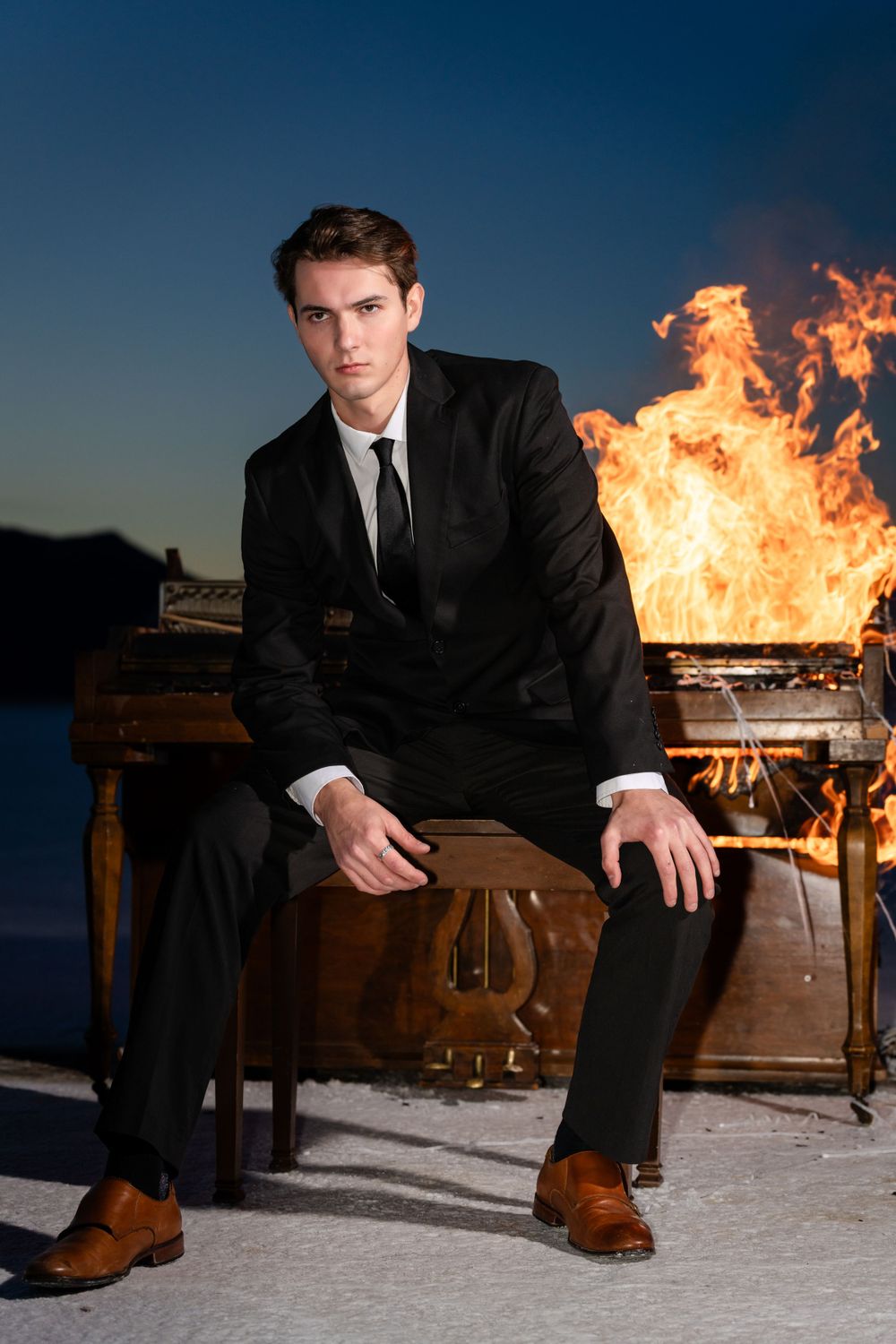Dark suit seated at burning piano creates dramatic desert scene.