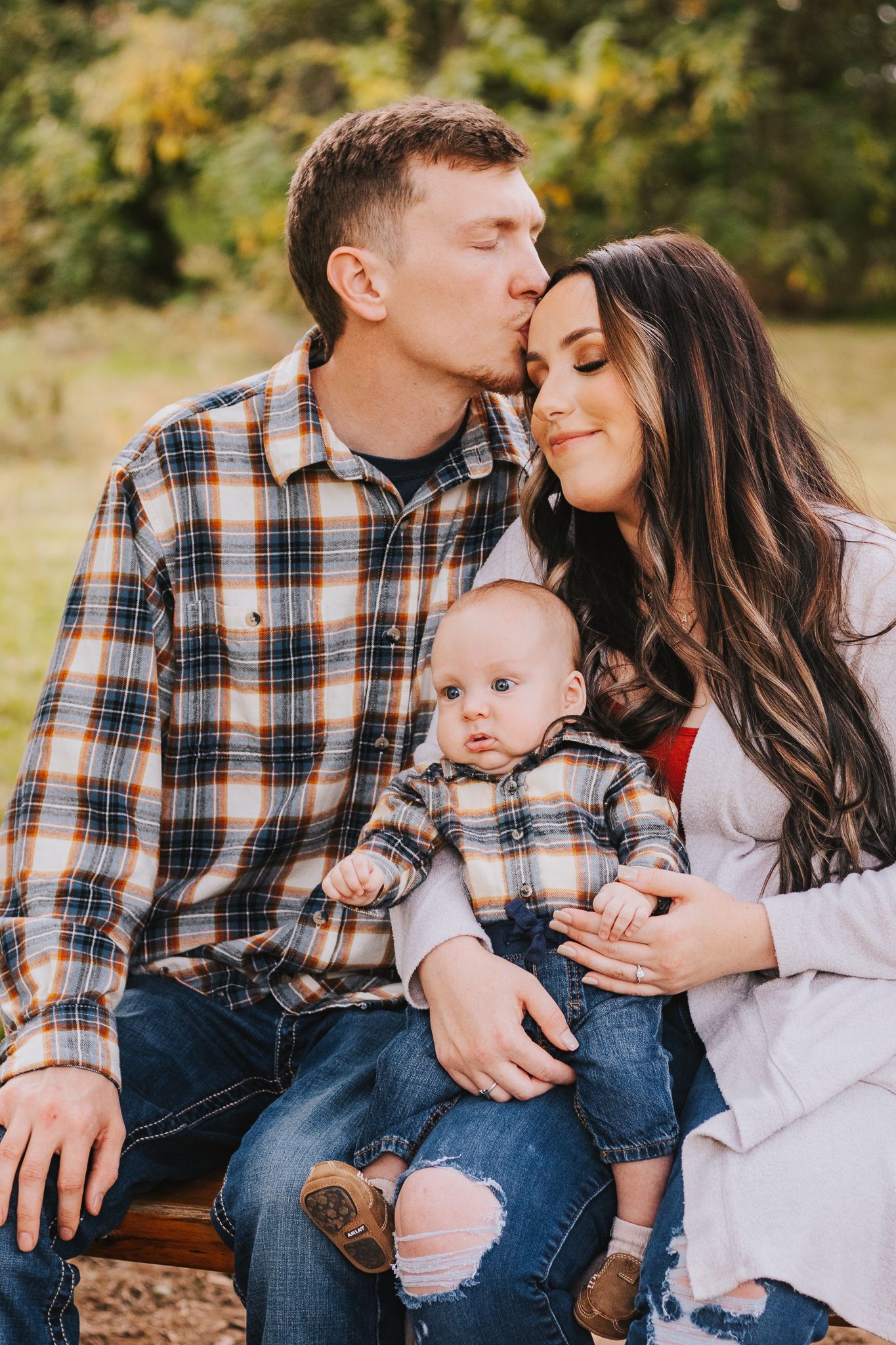 A tender family moment captured outdoors with parents and their baby in matching outfits.
