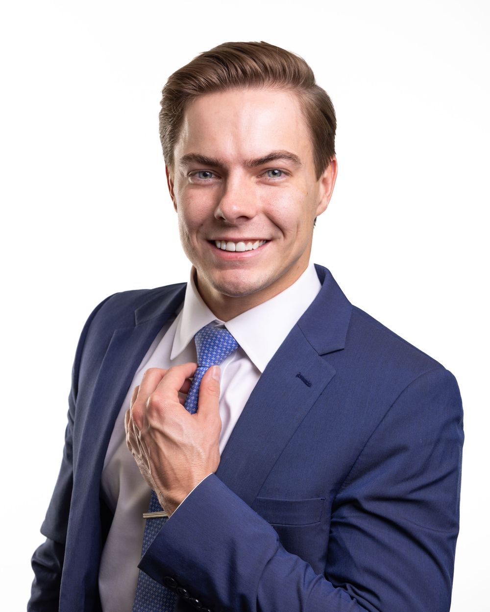 Business portrait of person in navy suit adjusting blue tie while smiling at camera.