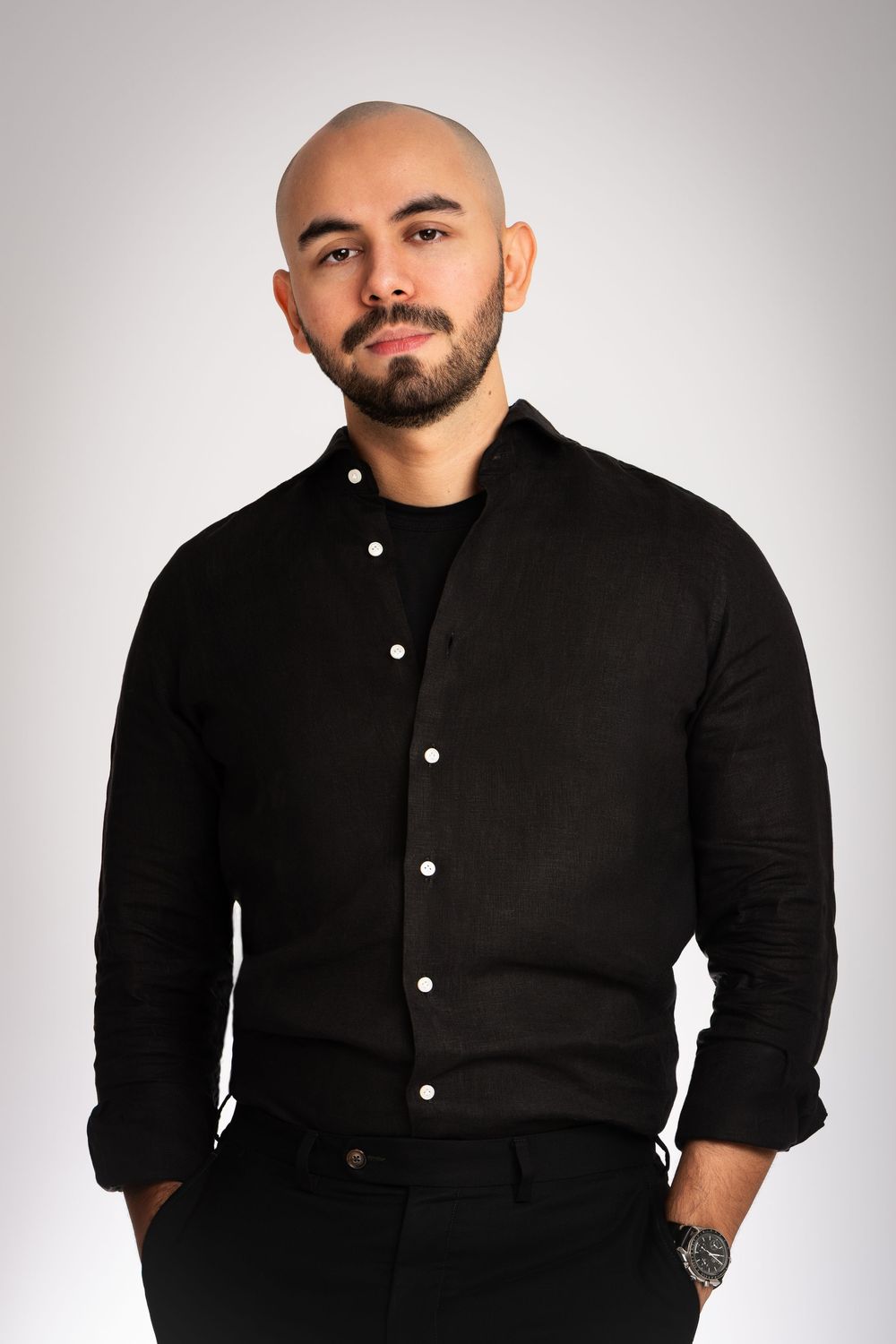 A corporate headshot of a person wearing a black button-up shirt posing against a white background in Cambridge, UK