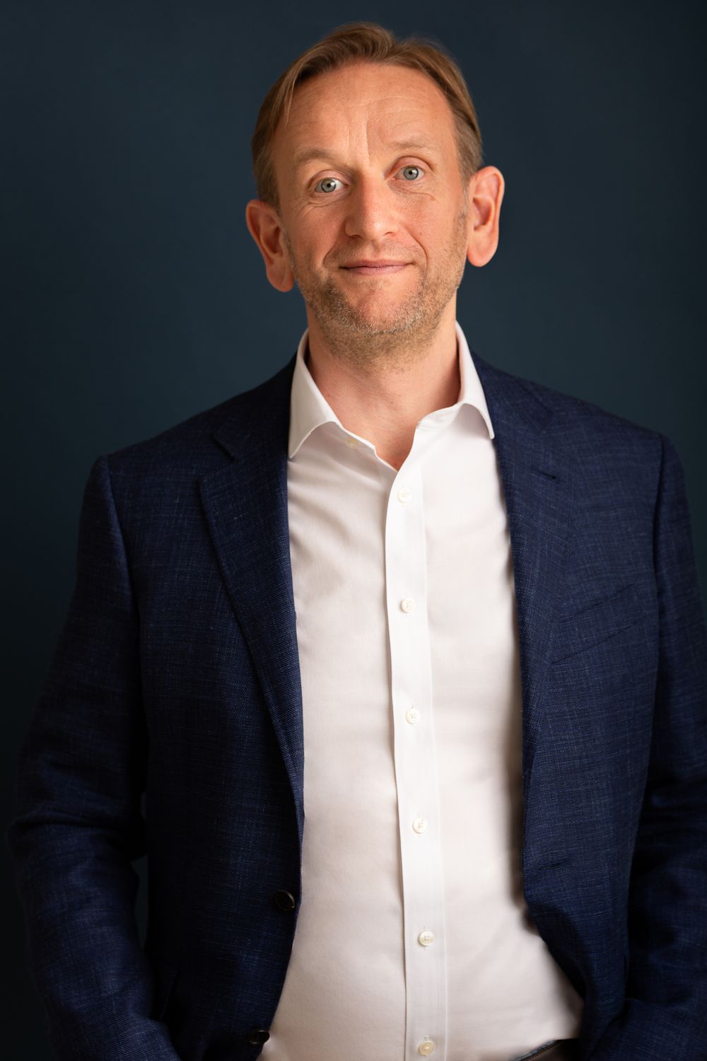 Corporate headshot against dark background showing person in navy blazer and white button-up shirt from different angles. Cambridge, UK