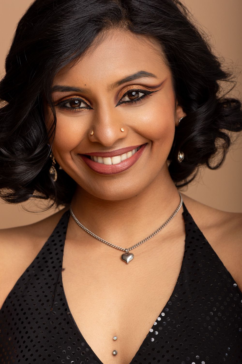 A headhshot of a lady with warm lighting features a radiant smile and a sleek black dress with a matching necklace accessory, Cambridge, UK