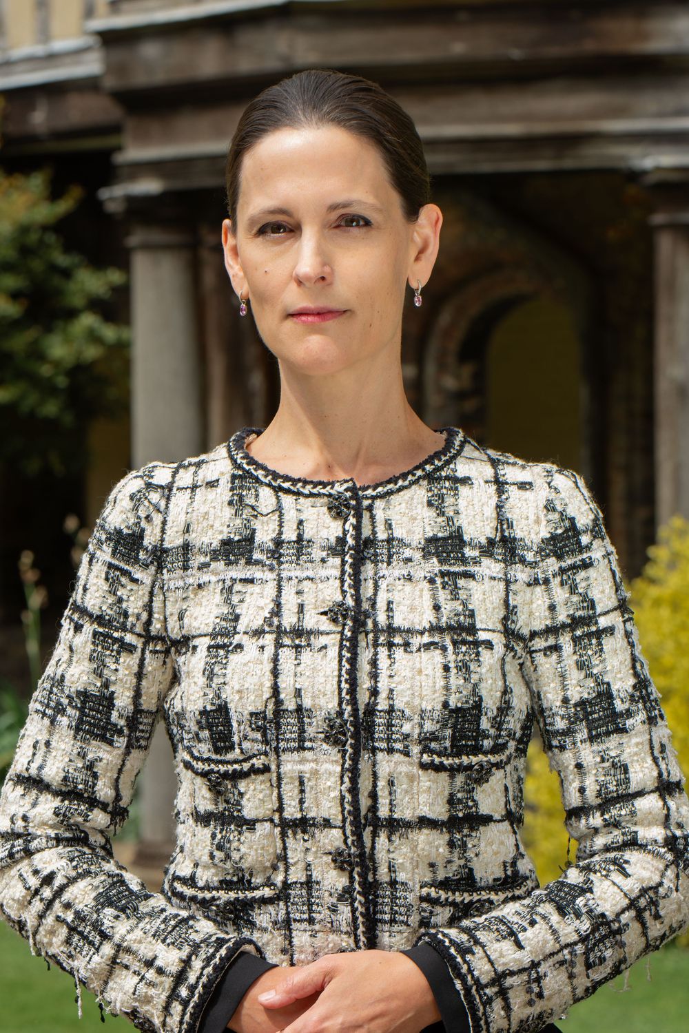 Professional headshot of a woman-professor wearing a black and white plaid tweed jacket with long sleeves in Cambridge University