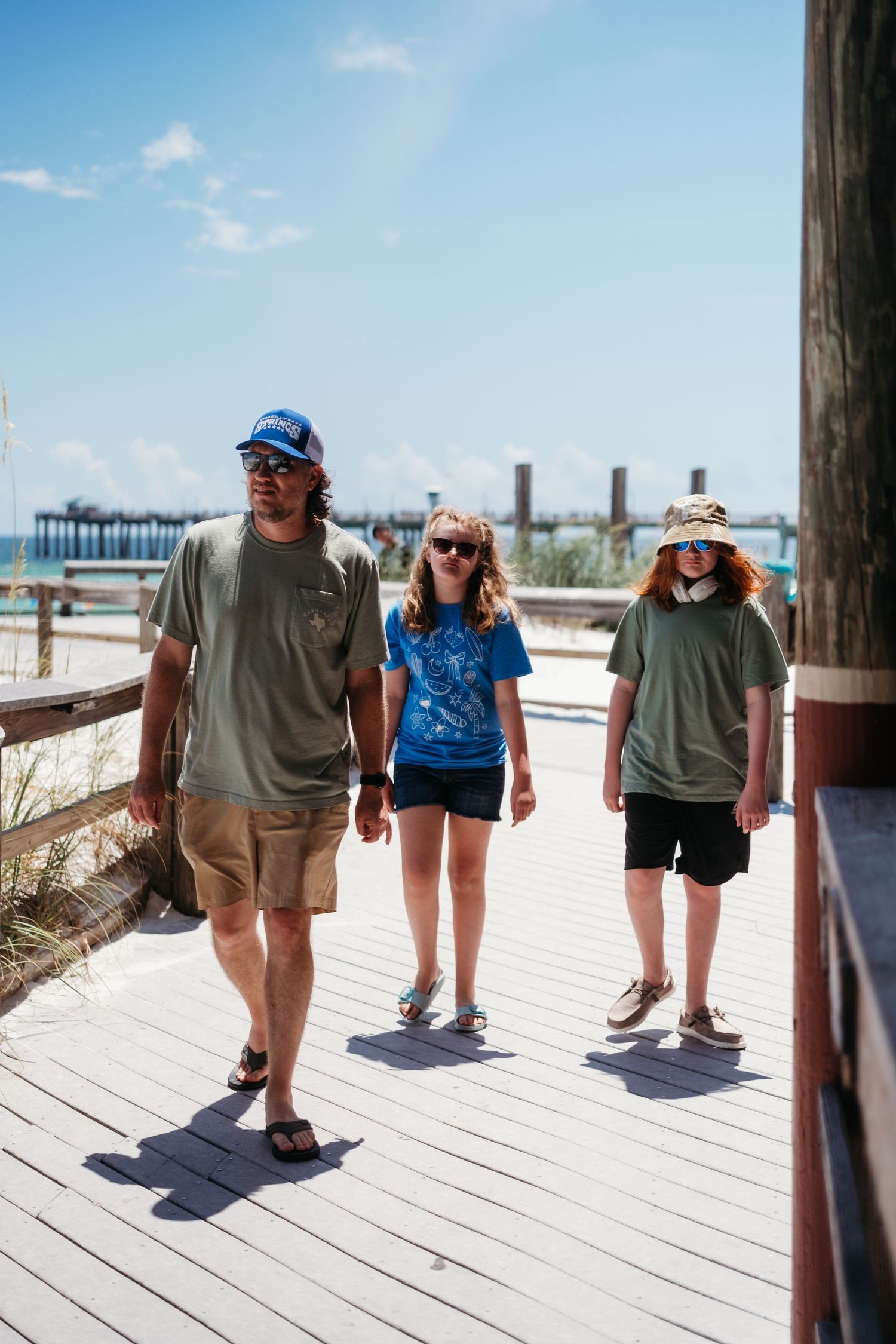 Family walking along a wooden boardwalk on a sunny summer day at the shore while wearing hats and sunglasses
