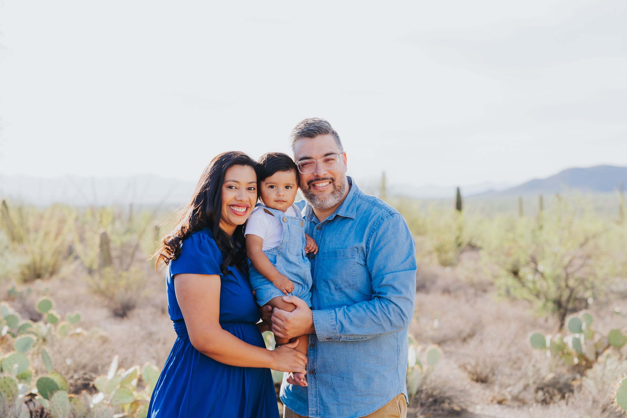 Family portrait session in a desert setting with mountains and saguaro cacti visible in the distance.