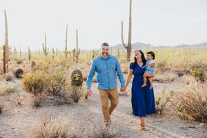 A family poses together in a desert landscape with towering saguaro cacti at sunset.