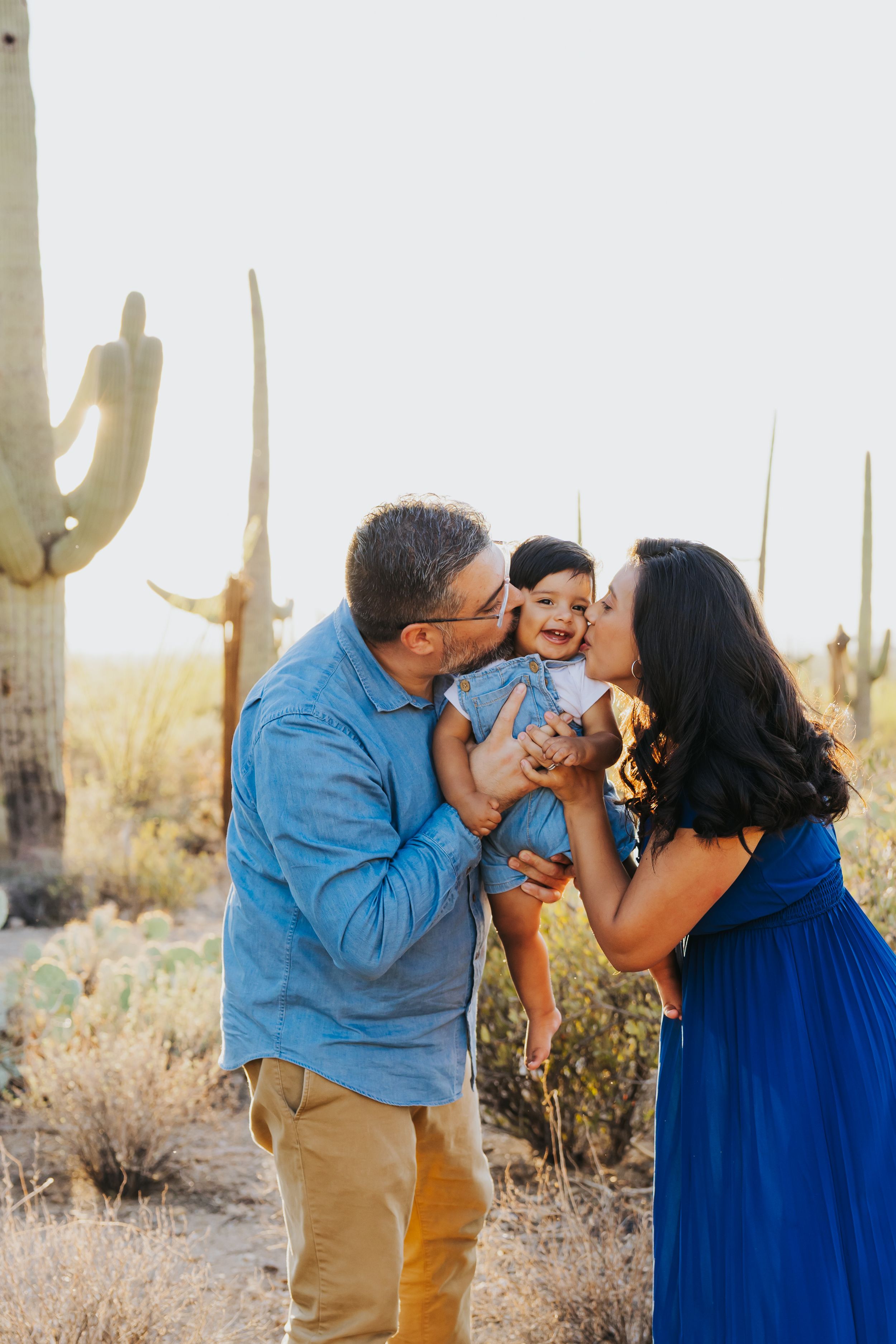 A loving family moment captured in the desert with saguaro cacti in the background.