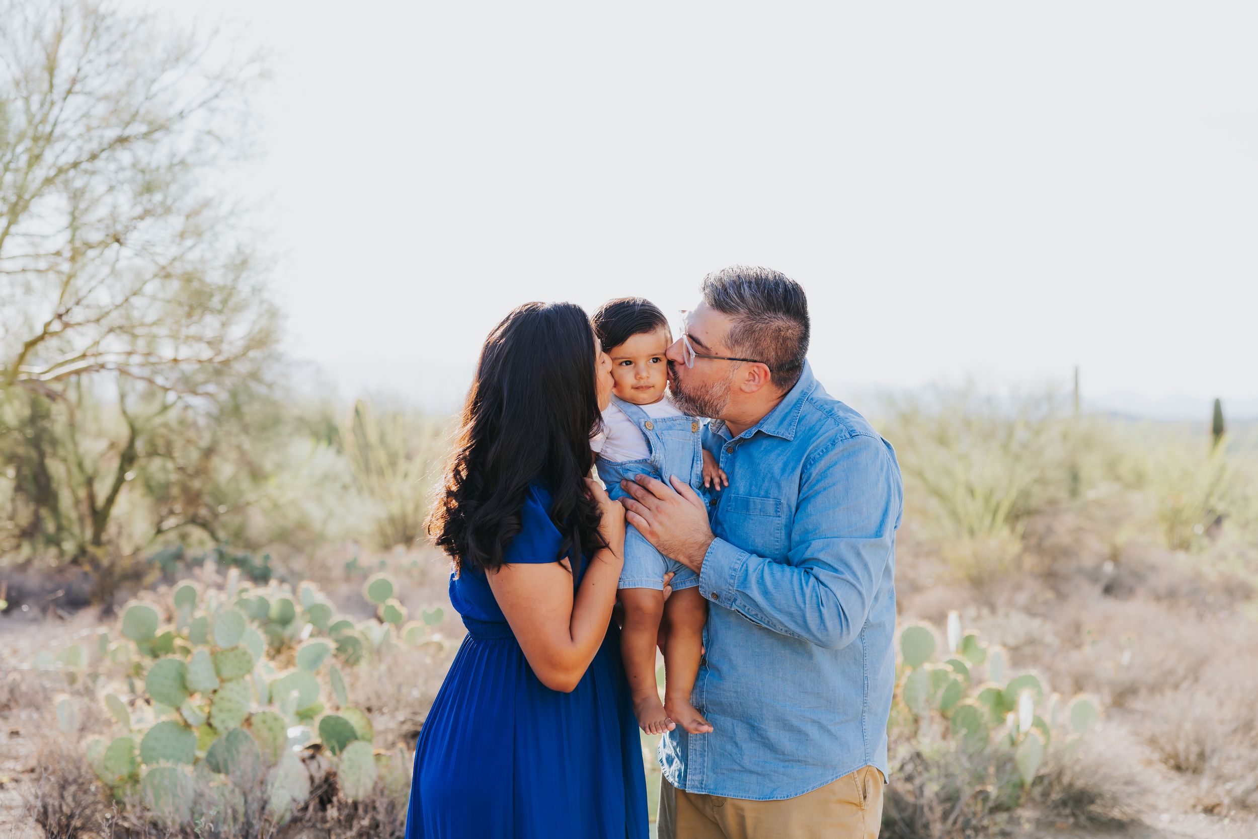A family shares tender moments together in a desert landscape with cacti and mountains in the background.