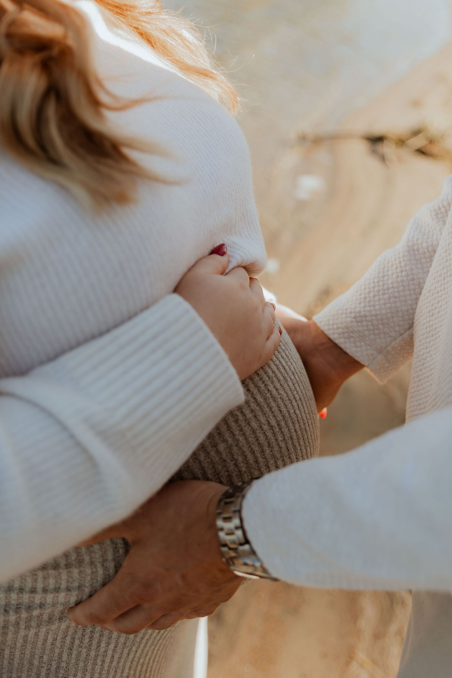 Close-up of hands wearing cozy white and beige sweaters showing a gentle embrace in warm lighting.