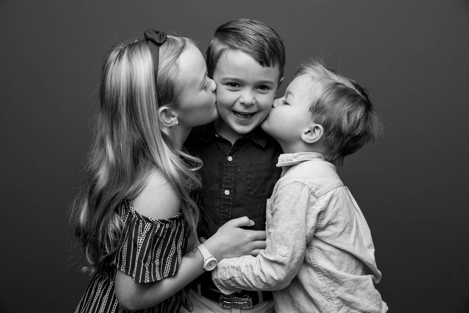 Black and white portrait of three children sharing a playful moment together.