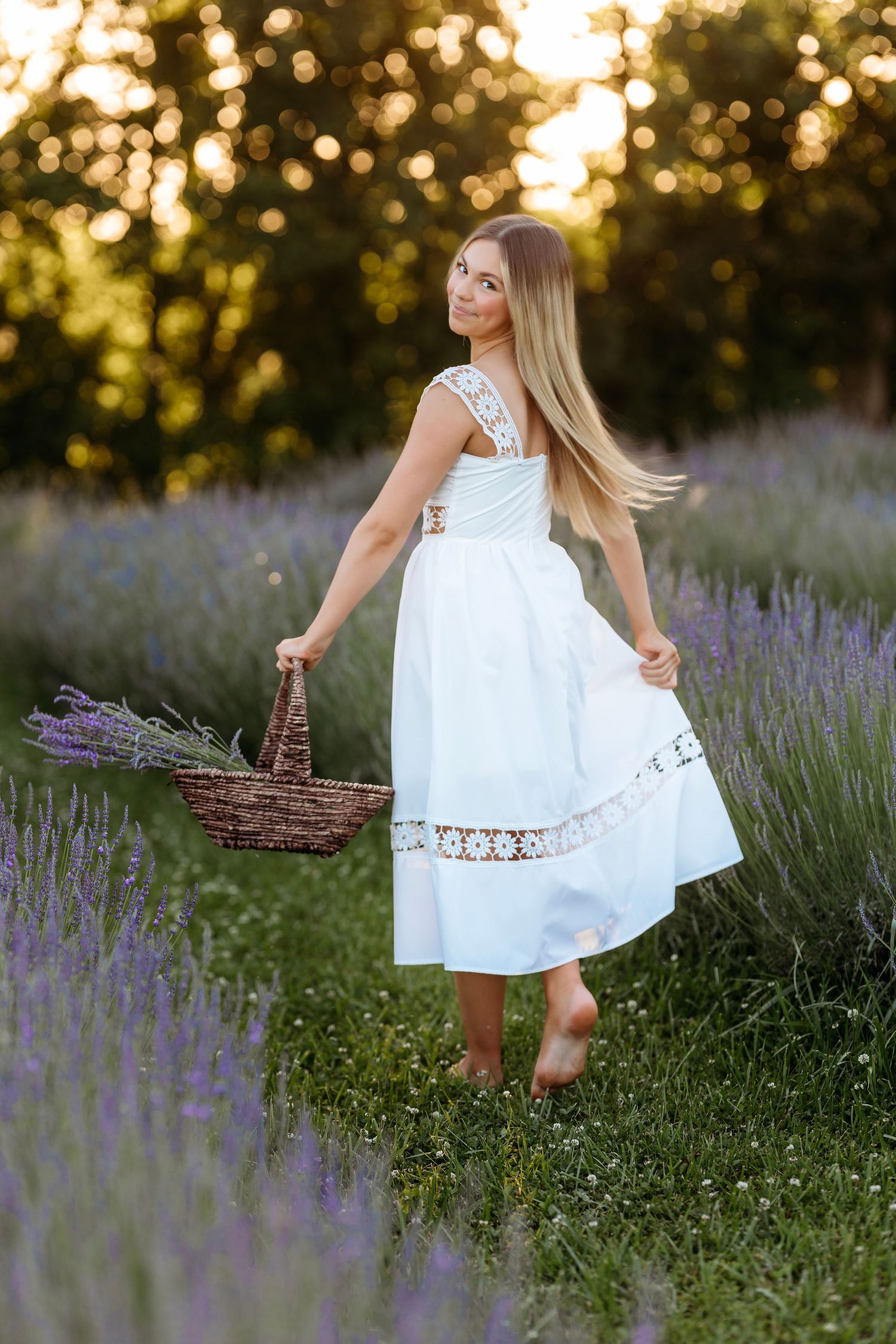 A teen in a white lace dress twirls in a lavender field at sunset while holding a woven basket.  Middle Tennessee Luxury Family Photographer