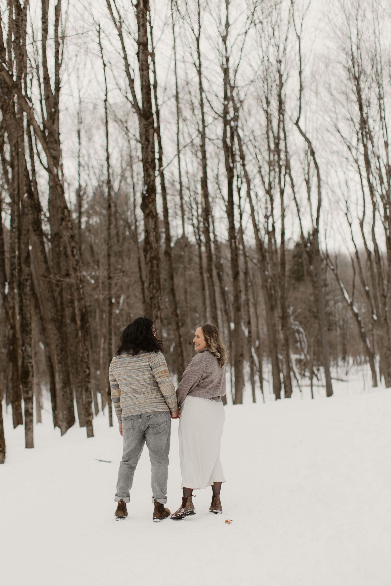 A couple walks through a snowy forest path in winter, holding hands and enjoying the serene winter landscape.