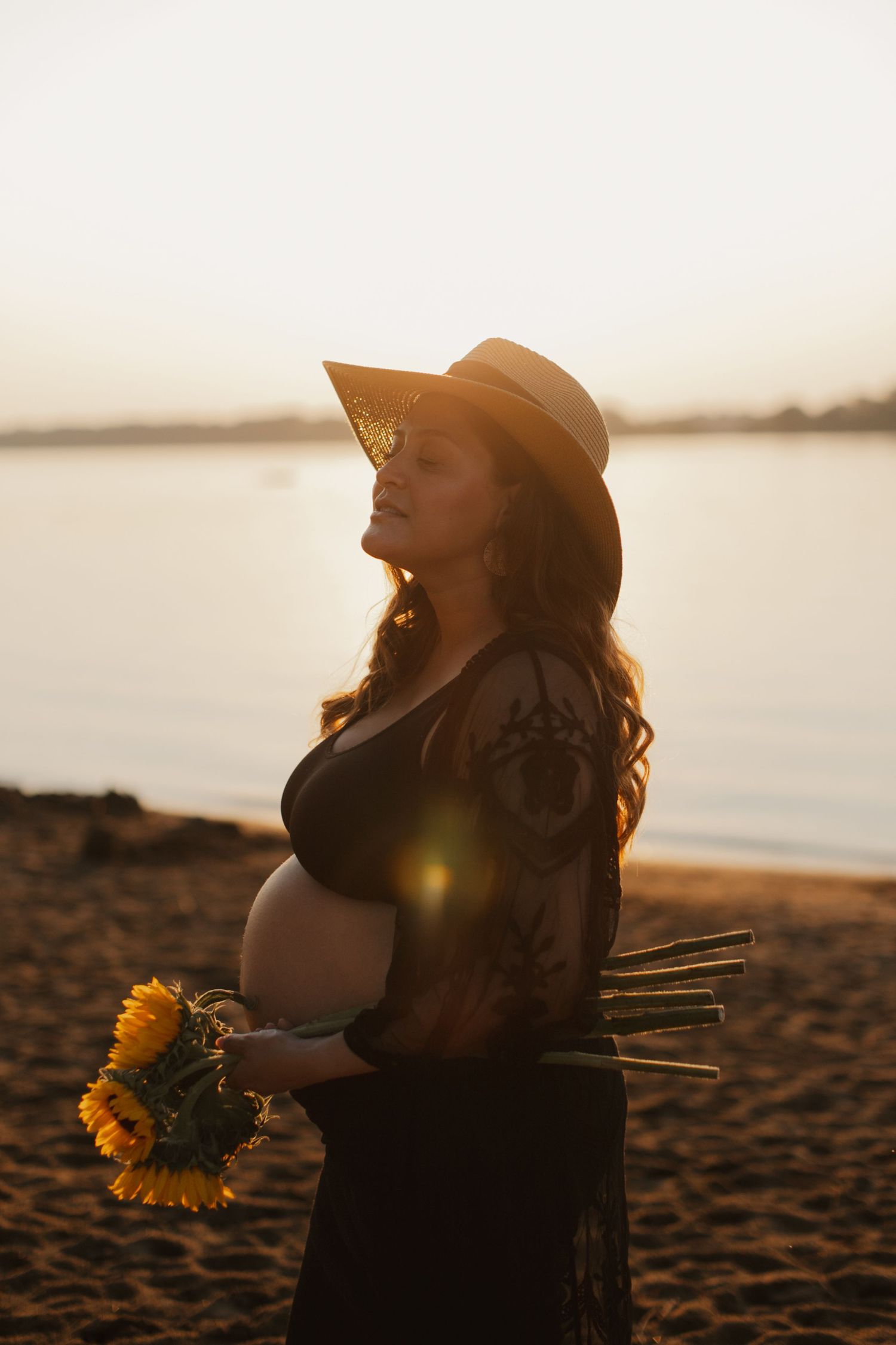Sunset maternity photo with sunflowers on beach.