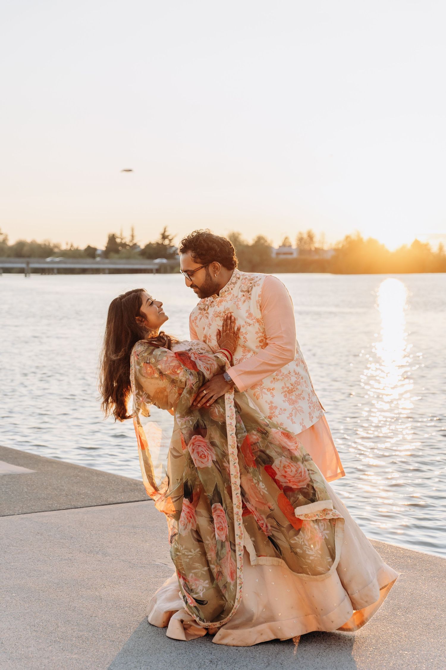 Couple sharing romantic moments at sunset by the waterfront in flowing outfits.