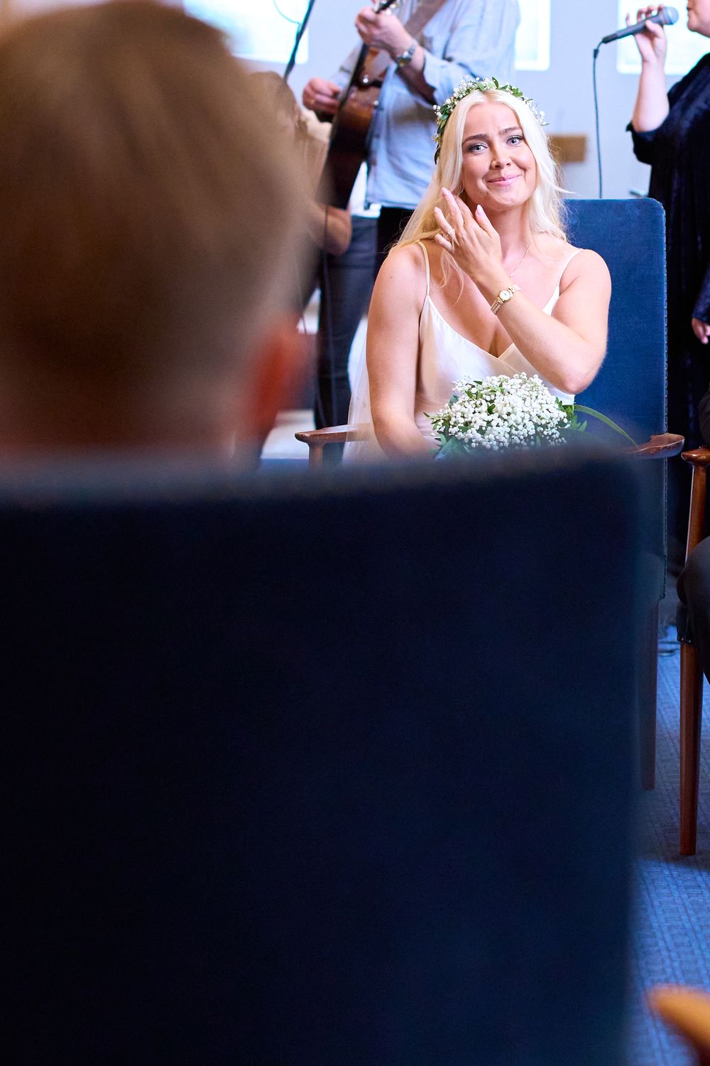 A bride in a white dress and floral crown sits emotionally during her wedding ceremony.