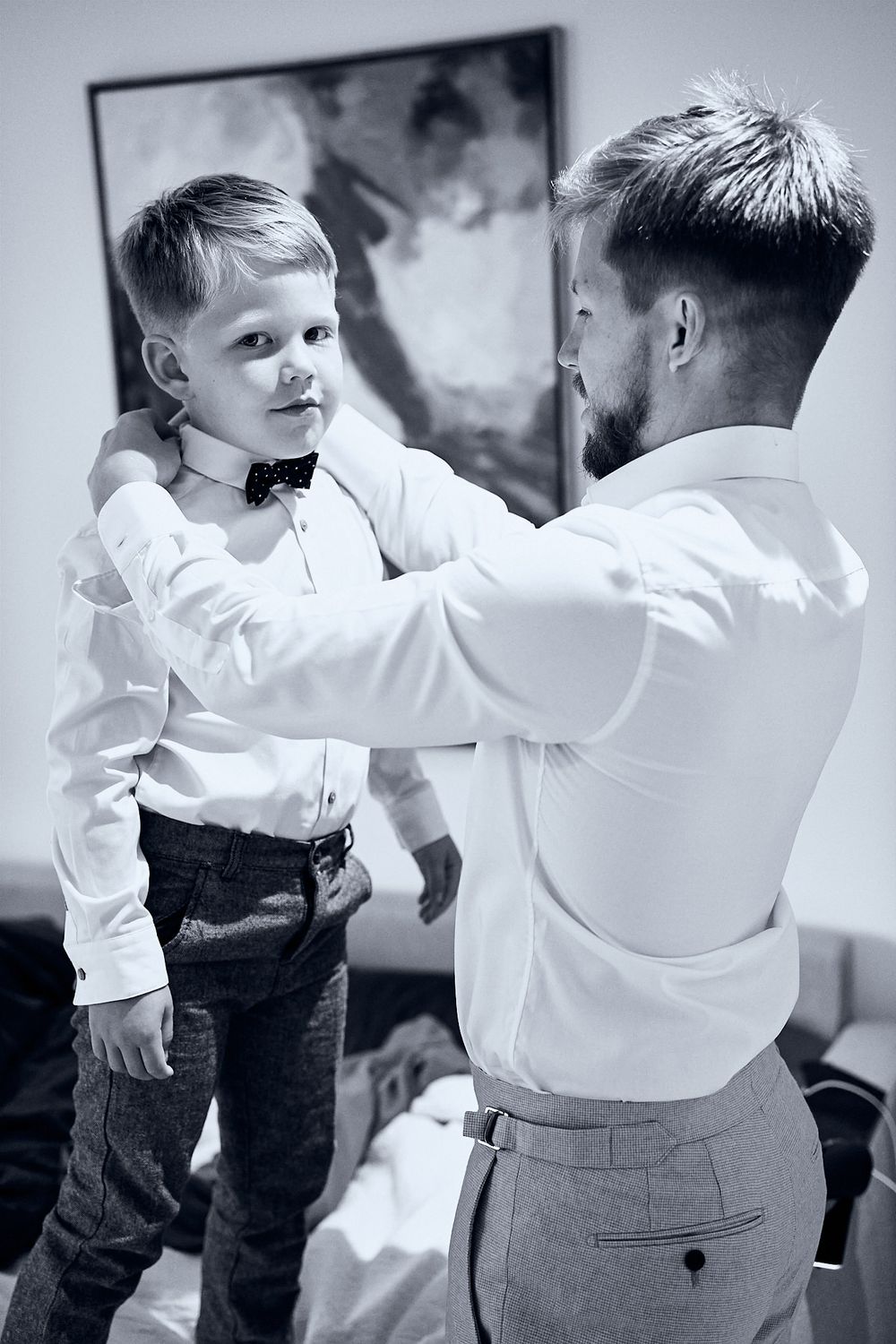 A tender black and white moment shows an adult helping adjust a young boy's bowtie before a formal occasion.