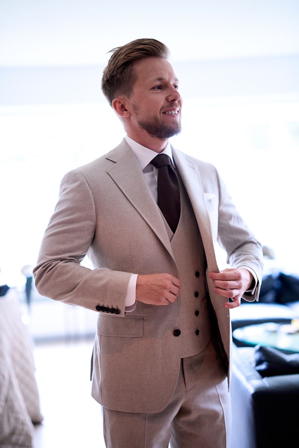 A beige three-piece suit with matching vest and dark tie styled for a formal occasion.