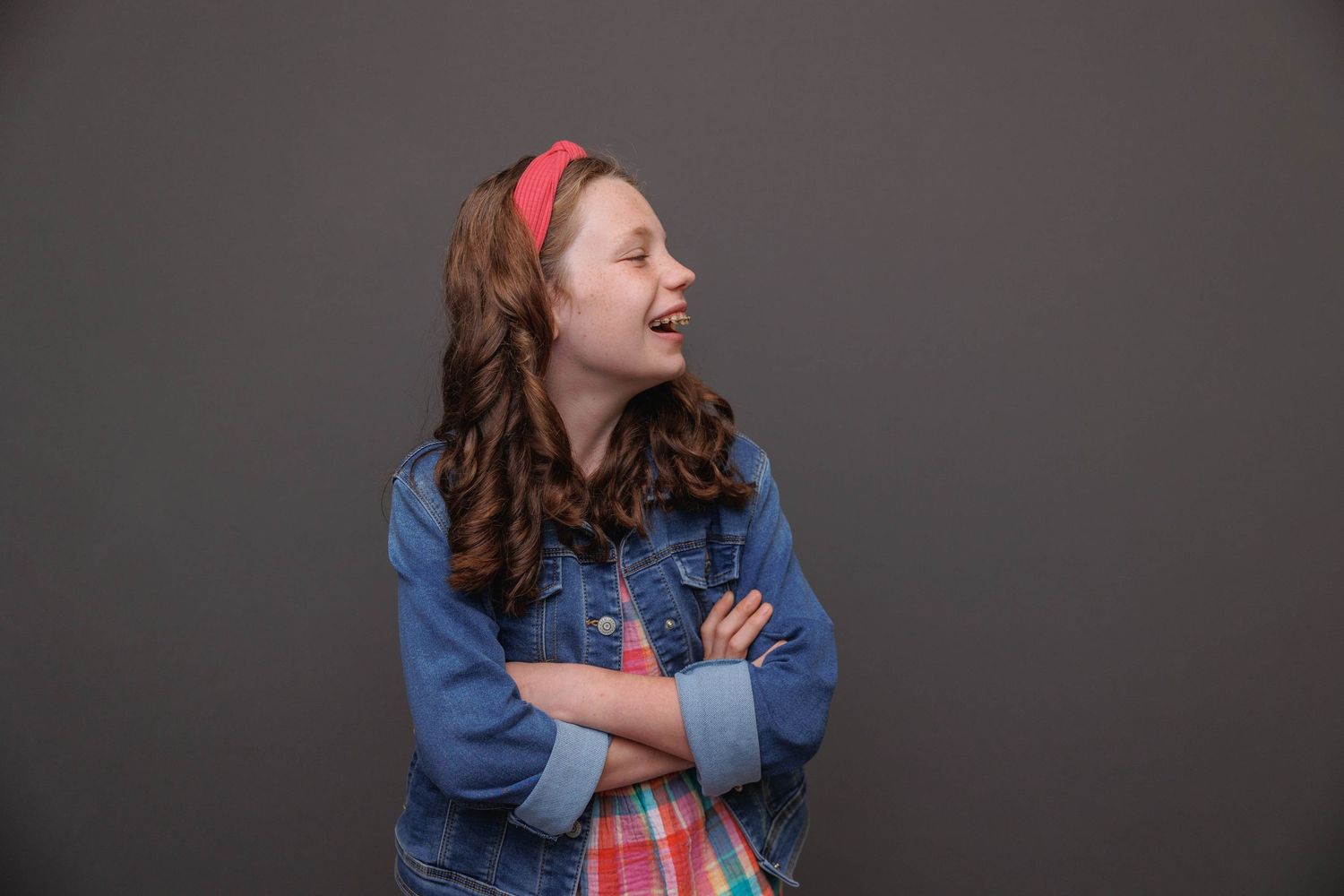 Portrait of a person in denim jacket with red headband looking to the side with crossed arms.