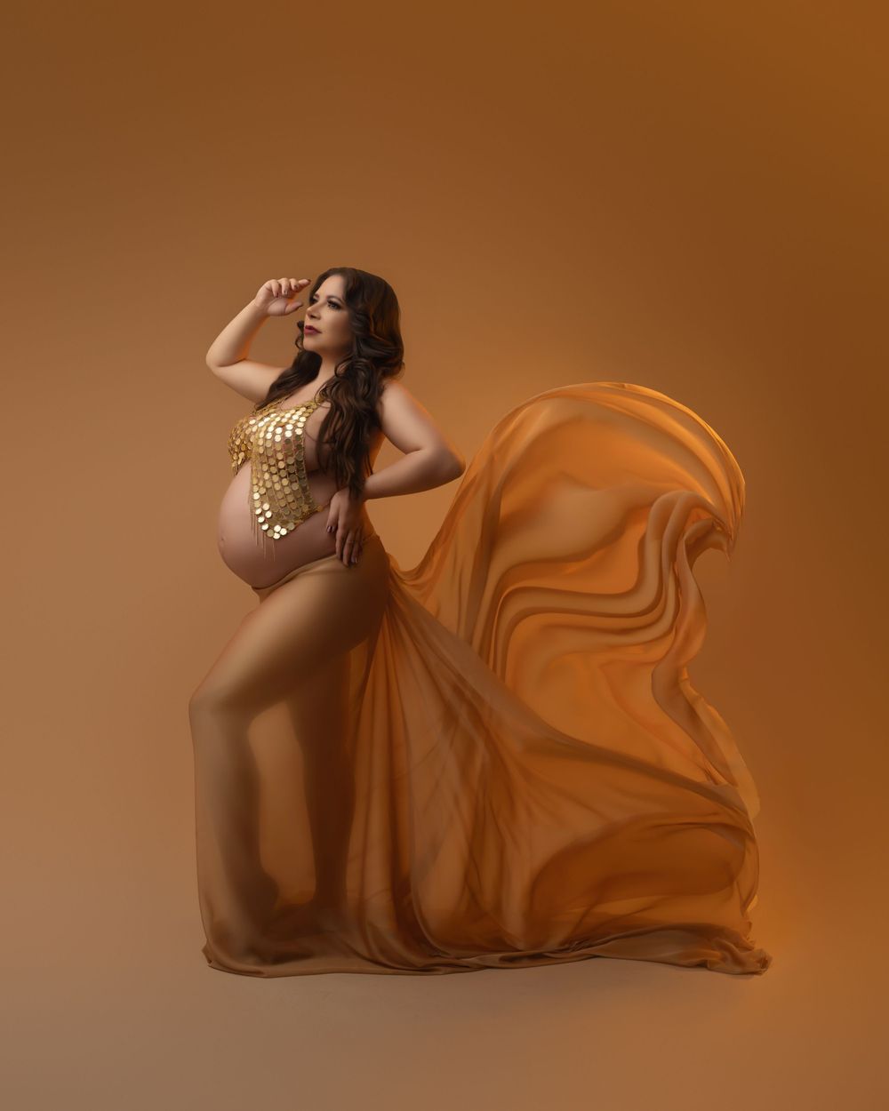Maternity photography featuring warm copper-toned flowing fabric against amber studio backdrop.