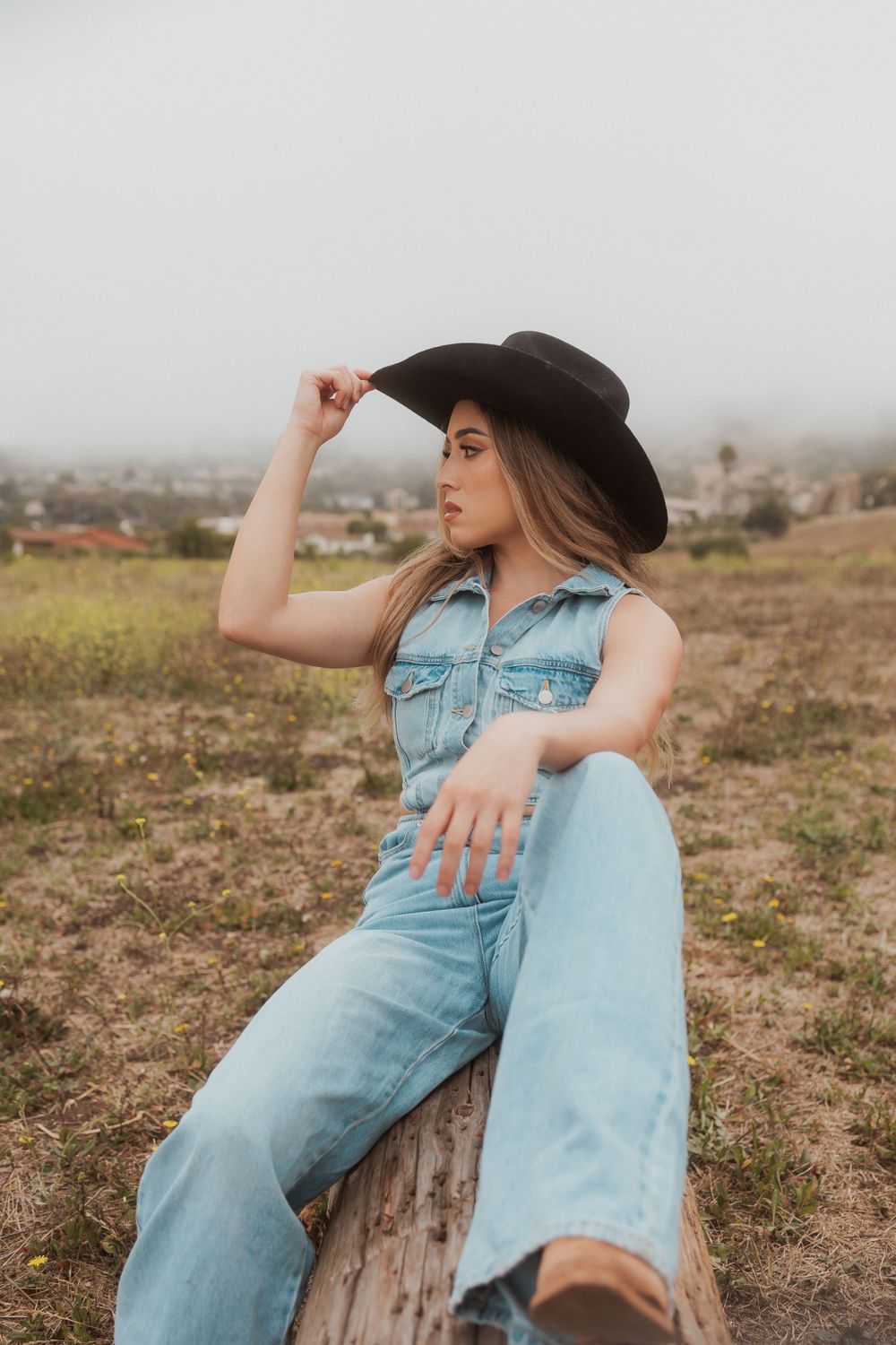 Western style portrait with denim vest and black hat against misty rural backdrop.