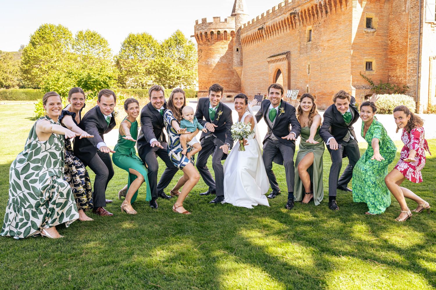 Wedding party striking fun poses on grass in front of a historic brick castle.