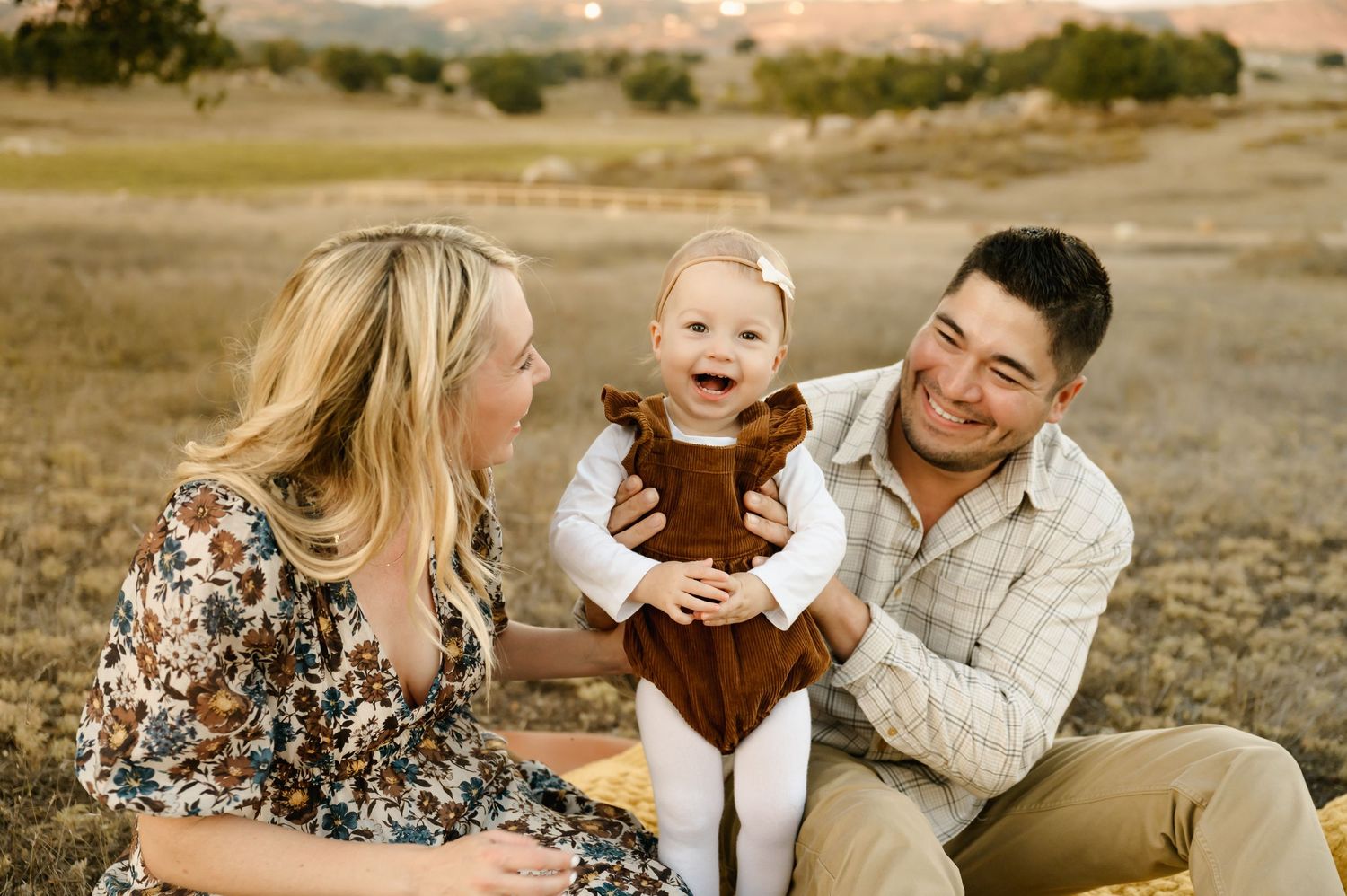 Family during Santa Barbara Photoshoot in grassy field with a smiling baby being held by the father.