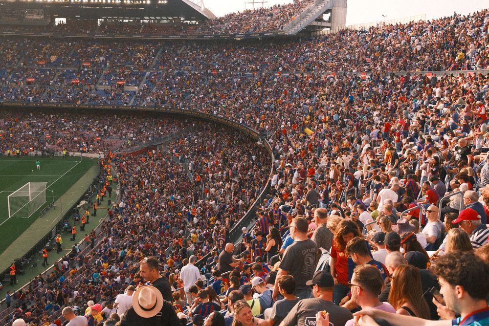 Packed stadium filled with spectators watching soccer match from steep grandstand seating.