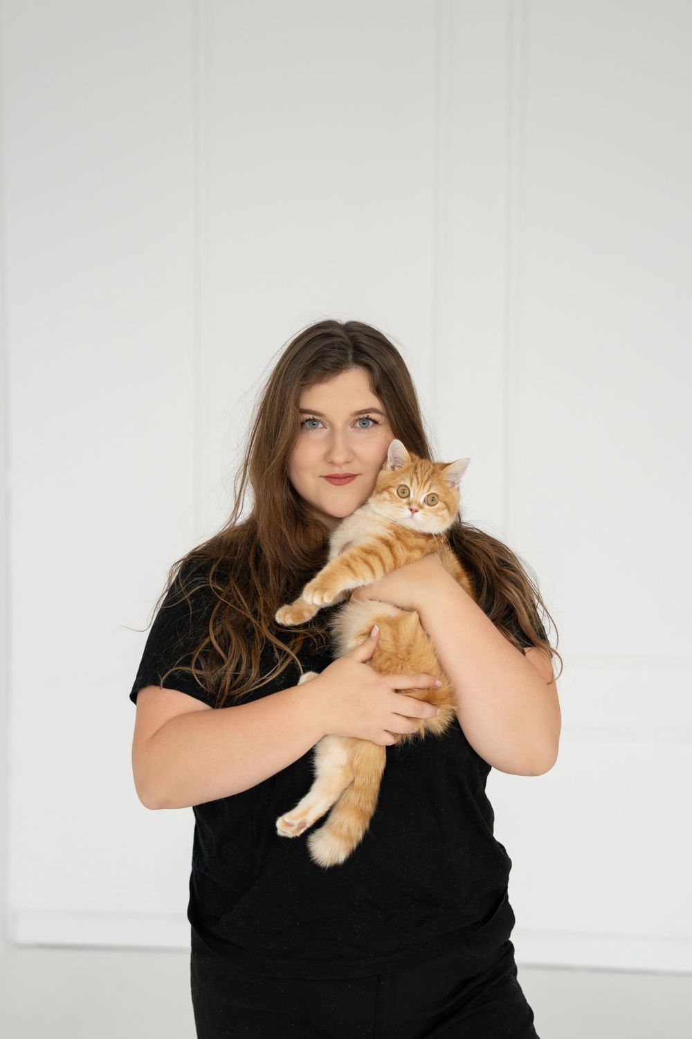 Person holding orange tabby cat while posing against white background.