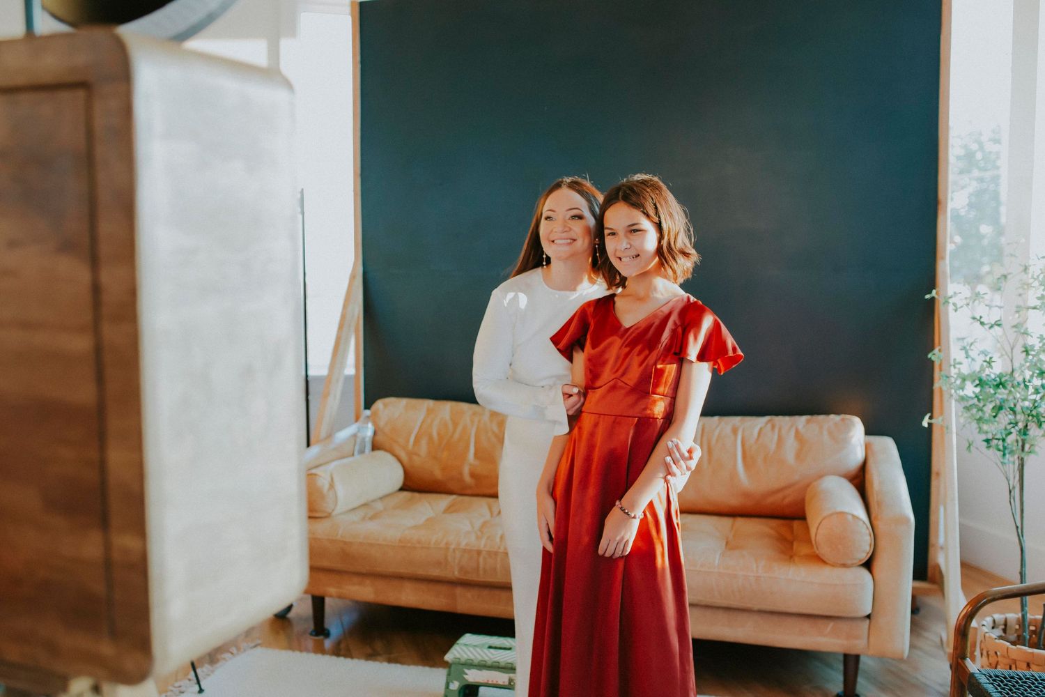 People in red dresses sharing laughter and embraces in a studio with wooden accents.
