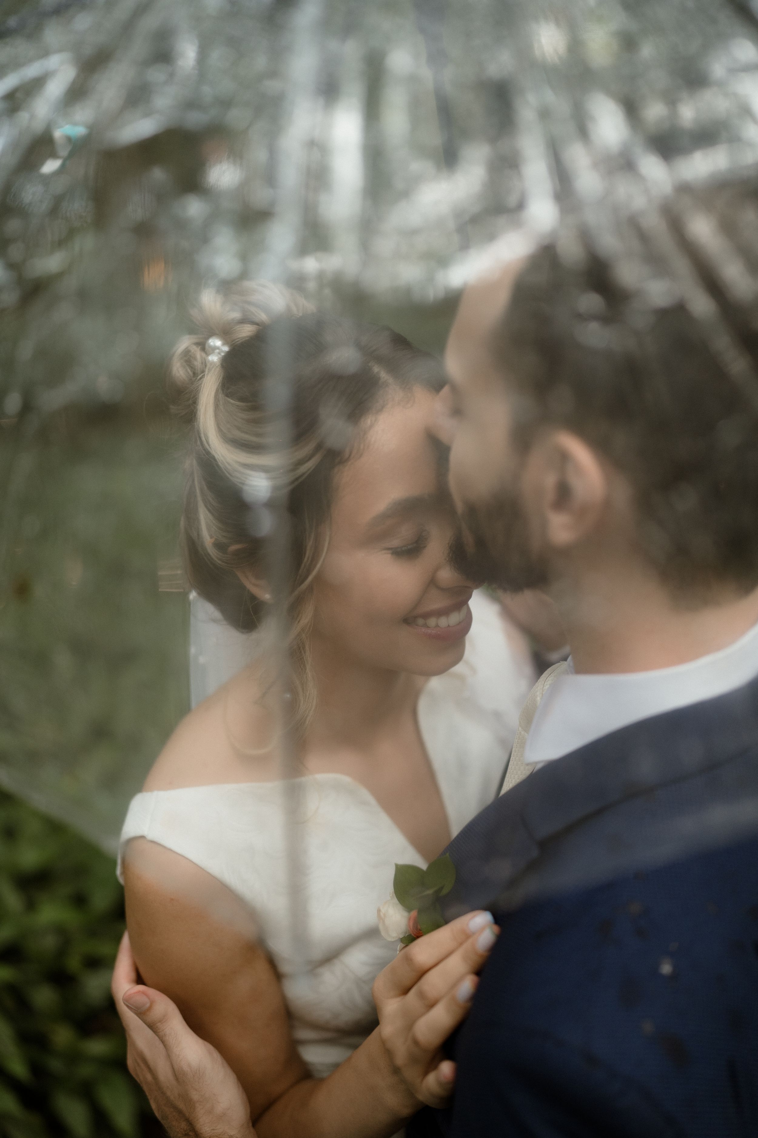 Intimate wedding moment captured through soft focus lens as couple embraces in romantic outdoor garden setting.