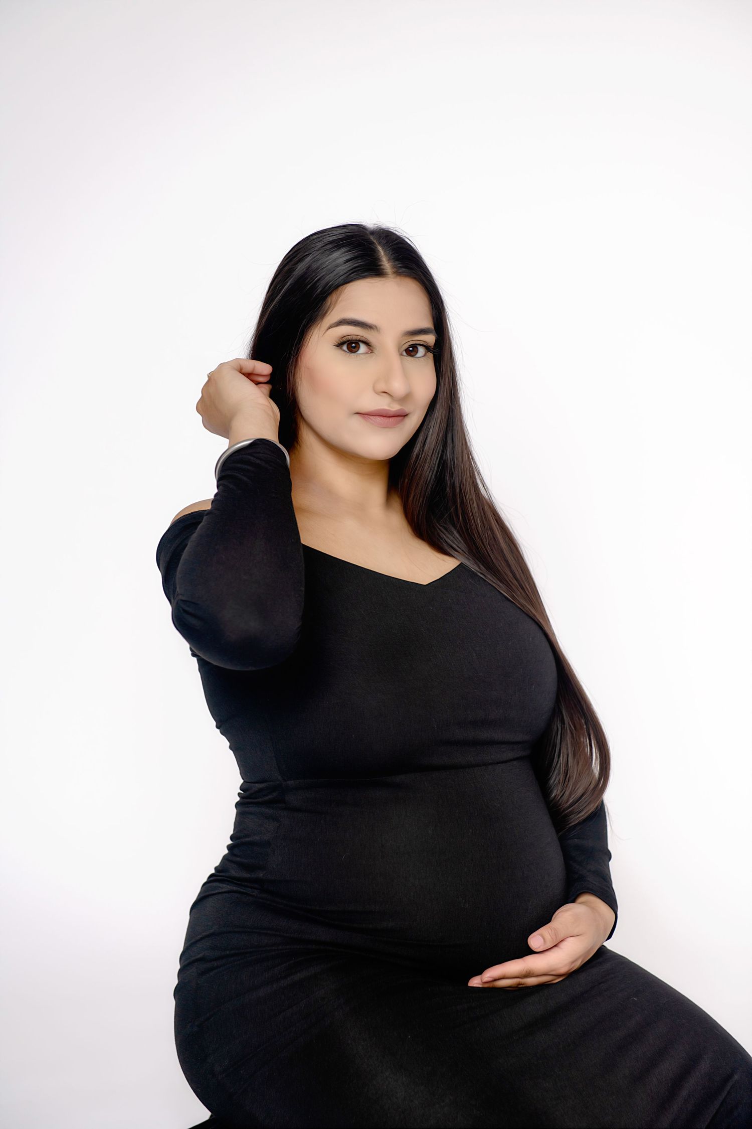 Maternity portrait of woman in black dress against white background.