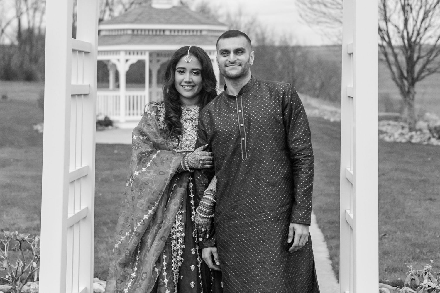 Couple in elegant ethnic wear standing together in a white gazebo.