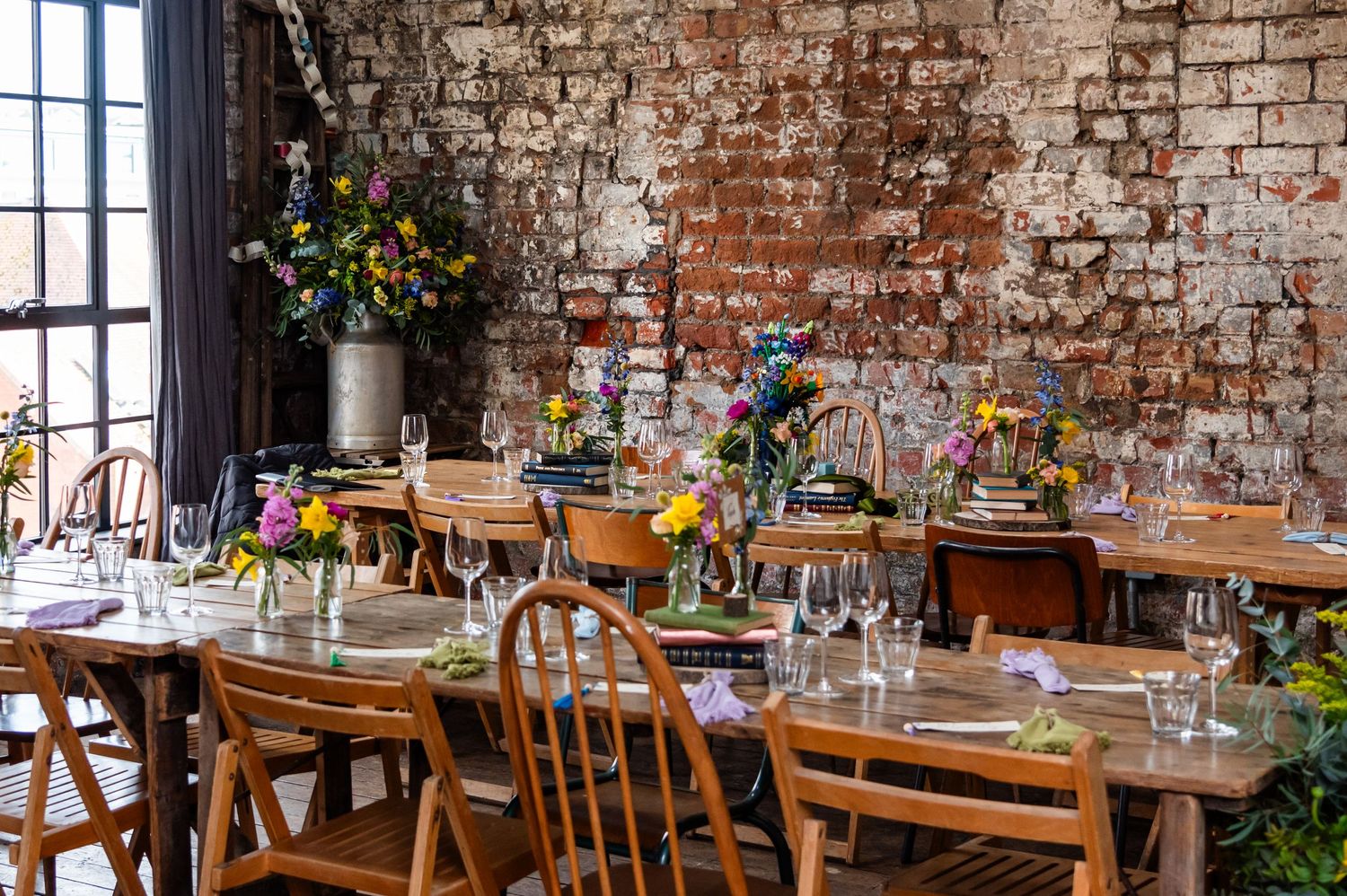 Reception venue with exposed brick walls, wooden chairs and colorful floral arrangements.