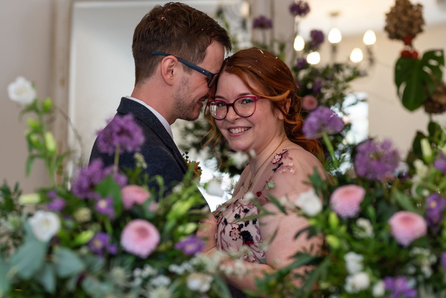 Romantic wedding scene surrounded by pink and purple floral decorations.