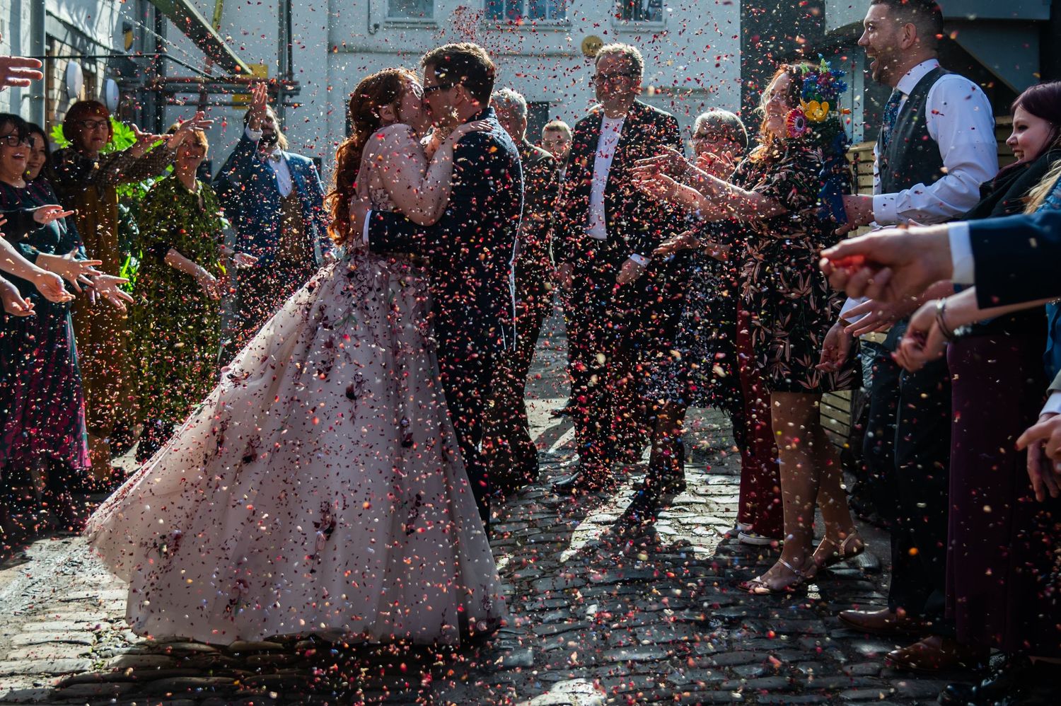 Wedding guests throw confetti in celebration at an outdoor ceremony.
