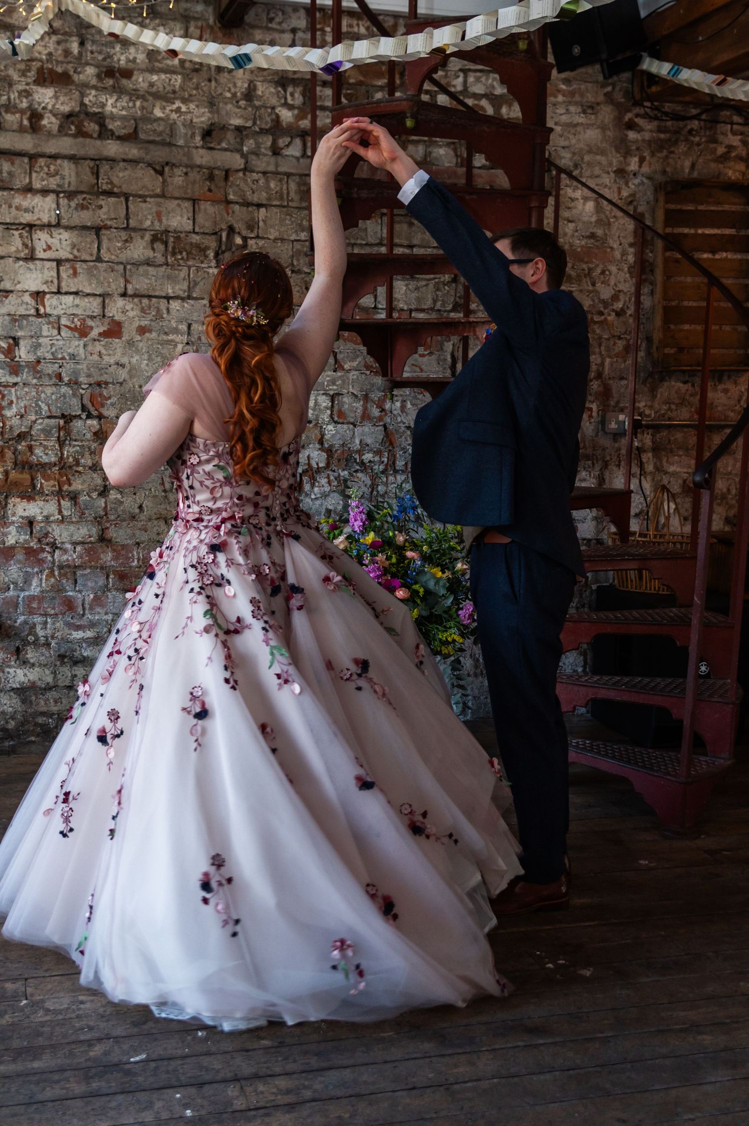 Couple dancing in a rustic brick venue with a floral decorated wedding dress.