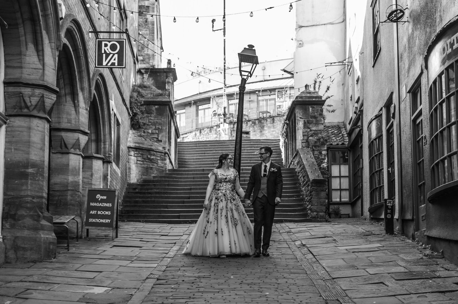 A wedding couple walks through a charming European cobblestone street with historic architecture.