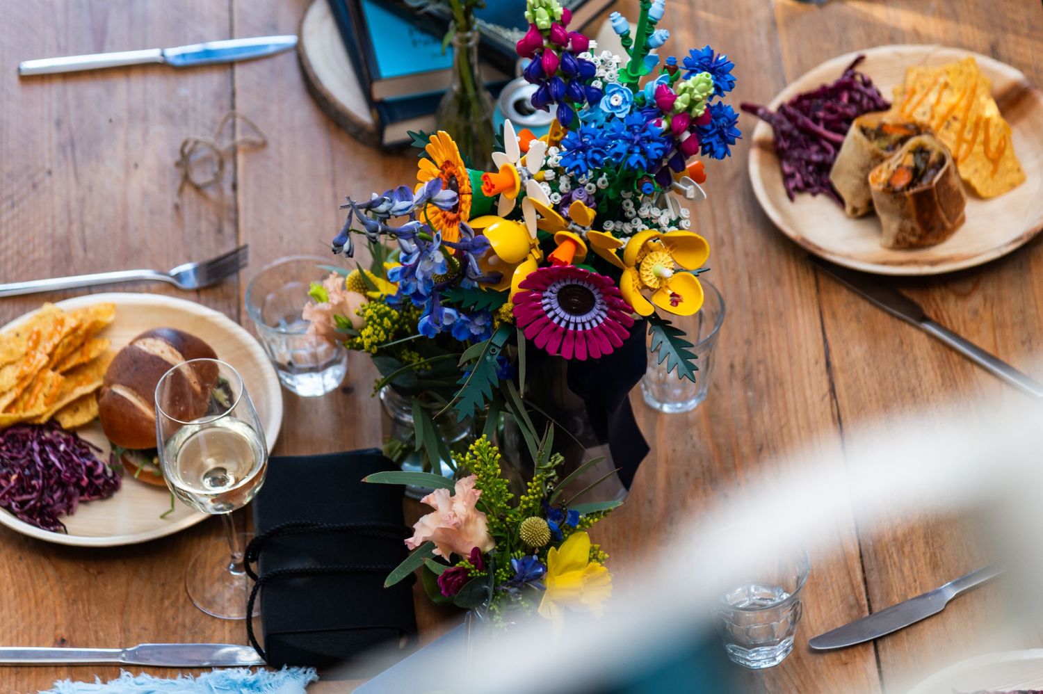 Rustic table setting with colorful floral centerpieces and glassware on a wooden surface.