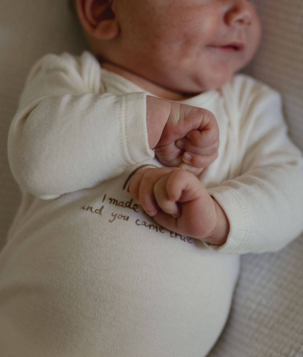 Close-up of infant wearing white sweater with text detail.